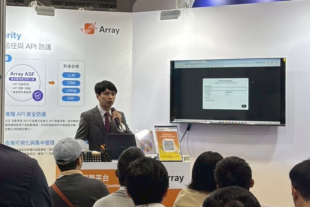 Peter Lu presenting with a microphone at the Array Networks booth, the API security architecture displayed on the backdrop behind him.